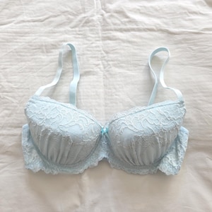 May include: A light blue bra with lace detailing. The bra has adjustable straps and a small bow in the center. The bra is made of a soft, delicate fabric and is designed for comfort and support.