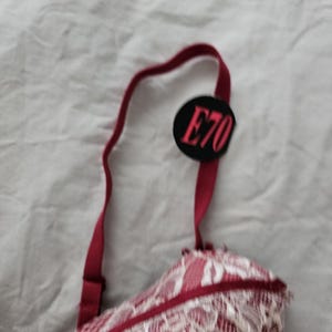 May include: A red and white lace bra with a tag that reads "E70". The bra features a delicate lace pattern and adjustable straps. The straps and trim are a deep red color.