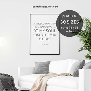 May include: A black and white printable wall art print with the text "As the deer longs for the streams of water, so my soul longs for you O God. Psalm 42:1". The print is framed and displayed on a white couch in a living room setting.