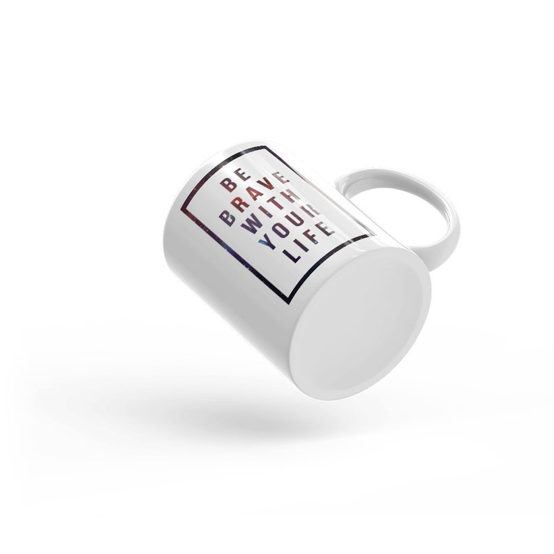 Pode incluir: Caneca de cer&acirc;mica branca com uma borda quadrada preta em torno do texto "BE BRAVE WITH YOUR LIFE". O texto est&aacute; em fonte branca com um fundo de gal&aacute;xia.