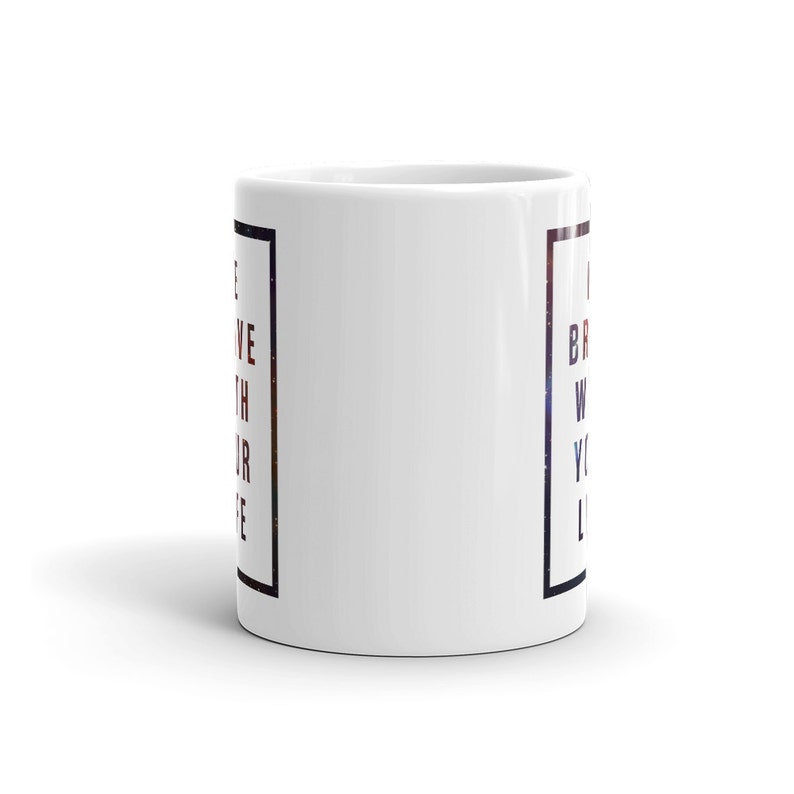 Pode incluir: Caneca de caf&eacute; de cer&acirc;mica branca com uma borda quadrada preta e o texto "Acredite com todo o seu cora&ccedil;&atilde;o" do lado esquerdo e "Seja corajoso com toda a sua vida" do lado direito. O texto est&aacute; em um degrad&ecirc; vermelho, branco e azul.