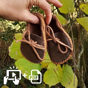 Puede incluir: Un par de mocasines de cuero marrón con cordones de cuero beige. Los mocasines están cosidos a mano y tienen un aspecto suave y cómodo.