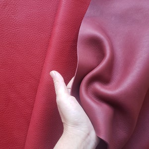 May include: Two pieces of leather in different shades of red. One piece is a deep red with a pebbled texture, while the other is a lighter, more burgundy shade with a smooth texture.