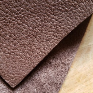 May include: Close-up of a brown leather fabric with a textured surface. The leather is folded over a brown fabric with a fuzzy texture.