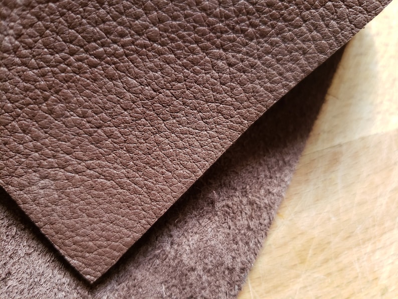 May include: Close-up of a brown leather fabric with a textured surface. The leather is folded over a brown fabric with a fuzzy texture.