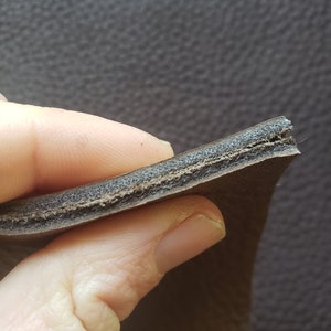 May include: Close-up of the cross-section of a brown leather strap, showing the layers of leather and a thin layer of padding.