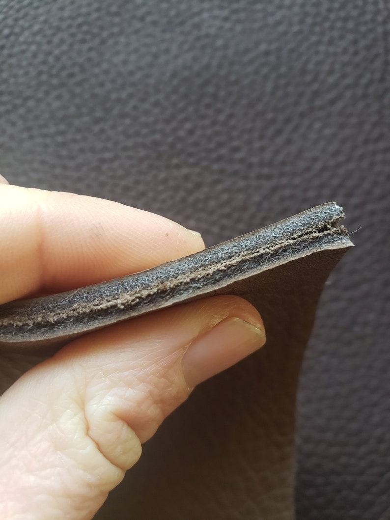 May include: Close-up of the cross-section of a brown leather strap, showing the layers of leather and a thin layer of padding.