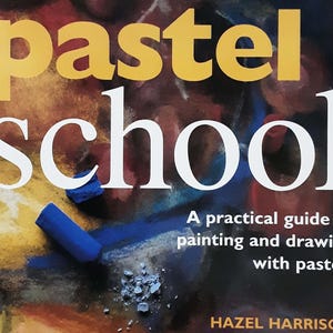 May include: A book cover with the title "pastel school" in large yellow and white letters. The subtitle reads "A practical guide to painting and drawing with pastels." A blue pastel stick and pastel dust are visible.