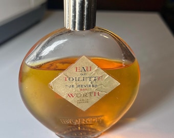 May include: A vintage glass bottle of "Je Reviens" Eau de Toilette by Worth Paris France. The bottle is round and clear with a gold cap. The label is diamond-shaped and features the text "Eau de Toilette" and "Je Reviens" in red.