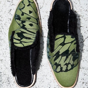 May include: A pair of green velvet slippers with a butterfly pattern and black fur trim. The slippers have a closed toe and a slip-on design.