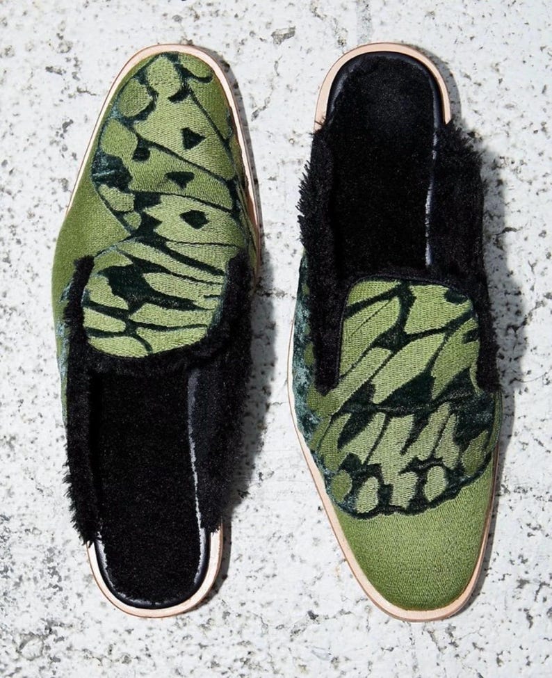 May include: A pair of green velvet slippers with a butterfly pattern and black fur trim. The slippers have a closed toe and a slip-on design.