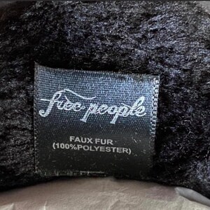 May include: Black faux fur label with white text that reads "Free People" and "Faux Fur (100% Polyester)"