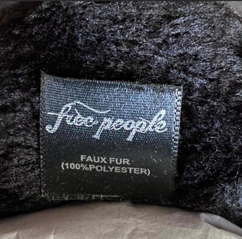 May include: Black faux fur label with white text that reads "Free People" and "Faux Fur (100% Polyester)"