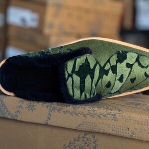 May include: Green velvet slipper with a black fur trim and an embroidered butterfly design.