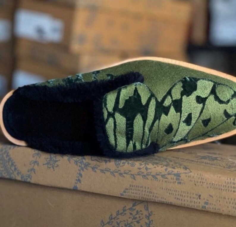 May include: Green velvet slipper with a black fur trim and an embroidered butterfly design.