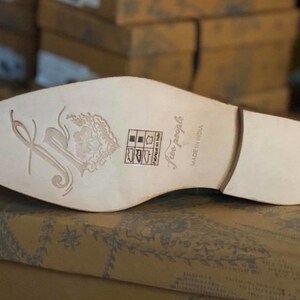 May include: The bottom of a light brown leather shoe with a white sole. The sole has a floral design and the text "Free People" and "Made in India".