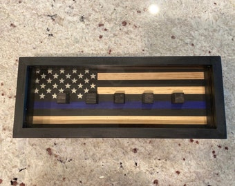 May include: A wooden shadow box with a thin blue line American flag design. The flag is made of wood and has a blue stripe with five black squares.