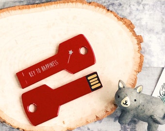 May include: Red key-shaped USB flash drive with the text "Key to Happiness" and a small star design. The drive is sitting on a wooden surface.