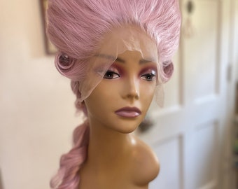May include: A pink wig with a high, bouffant style and a long braid. The wig is styled in a classic, elegant fashion.