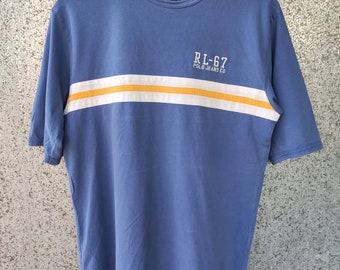 May include: A blue short-sleeved t-shirt with a white and yellow stripe across the chest. The shirt has the text "RL-67 Polo Jeans Co." printed on the stripe.