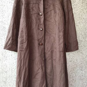 May include: A brown long-sleeved coat with a collar and button closure. The coat has a textured fabric and a label that reads "TADASHI" in white text on a green background.