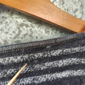May include: Close-up of a dark gray knit shirt with horizontal white stripes. The shirt is hanging on a wooden hanger. The fabric appears soft and textured.