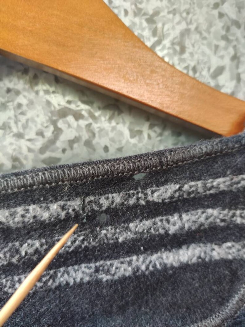 May include: Close-up of a dark gray knit shirt with horizontal white stripes. The shirt is hanging on a wooden hanger. The fabric appears soft and textured.