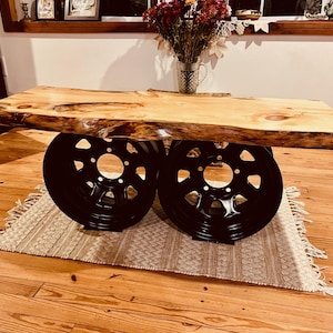 May include: A rustic coffee table made from a live edge slab of wood with a natural wood finish. The table is supported by two black painted wheels.