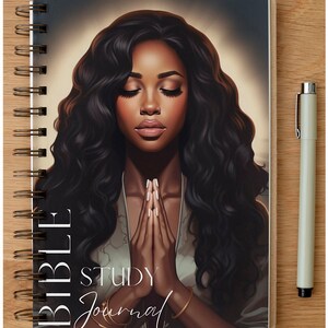 Op de afbeelding: Een zwart-wit spiraalgebonden notitieboek met een kleurrijke illustratie van een vrouw met haar handen gevouwen in gebed. De tekst "Bible Study Journal" staat op de voorzijde.