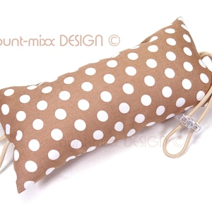 以下が含まれることがあります： 白のドット柄の茶色のドアストッパーで、ベージュの紐で閉じられています。ドアストッパーは布製で、透明なプラスチックの留め具が付いています。