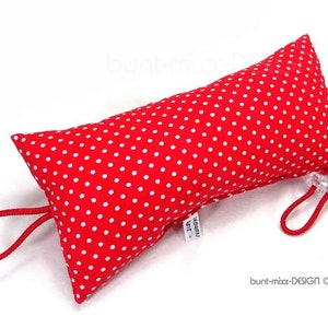 Könnte beinhalten: Ein rotes, längliches Kissen mit weißen Punkten. An jedem Ende sind rote Kordeln angebracht, die mit einem transparenten Kunststoffverschluss befestigt sind. Das Kissen hat eine leuchtend rote Farbe.