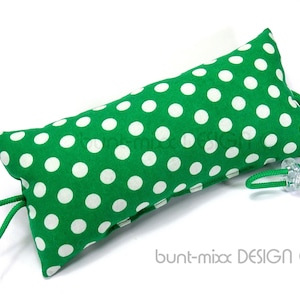 Pode incluir: Um calço de porta verde com bolinhas brancas, fecho de cordão e um botão de plástico transparente.