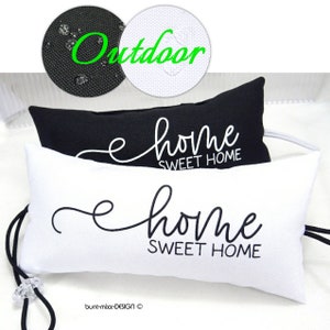 Op de afbeelding: Twee rechthoekige buitenkussens, één zwart en één wit, elk met de woorden "home SWEET HOME" in een cursief lettertype. Het woord "Outdoor" staat in het groen boven de kussens. De kussens hebben een trekkoord en een doorzichtige kraal.