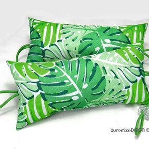 Könnte beinhalten: Zwei grüne und weiße Kissen mit tropischem Blatt-Muster. Die Kissen sind mit einer grünen Schnur zusammengebunden.