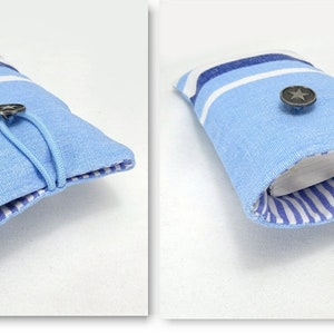 以下が含まれることがあります： 白と青のストライプ柄の薄い青色の布製のポーチ。ポーチはボタン留めと青い紐が付いています。ポーチが開いていて、白と青のストライプの裏地が見えています。