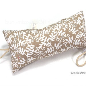 Könnte beinhalten: Ein beiger Türstopper mit einem weißen Blumenmuster. Der Türstopper hat an einem Ende eine Schlaufe und am anderen Ende einen Plastikclip.