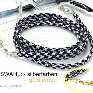 Könnte beinhalten: Schwarz-weiße gemusterte Brillenkette mit silbernen oder goldenen Verschlüssen. Die Kette ist aus Stoff und hat ein Hahnentrittmuster. AUSWAHL: - silberfarben - goldfarben