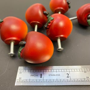 May include: Six red apple-shaped cabinet knobs with silver screws. The knobs are approximately 2.5 cm in diameter.