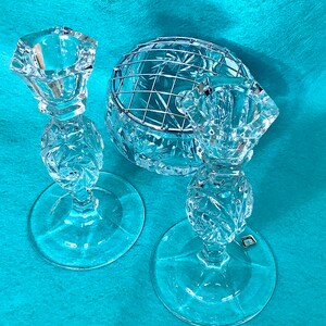 May include: Two crystal candle holders with a crystal bowl with a wire insert. The candle holders have a starburst pattern and the bowl has a floral pattern.