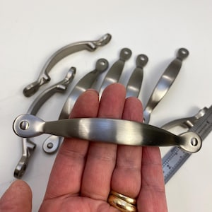 Peut inclure: Un ensemble de huit poignées de cabinet en nickel brossé avec un design incurvé. Les poignées mesurent environ 7,5 cm de long.