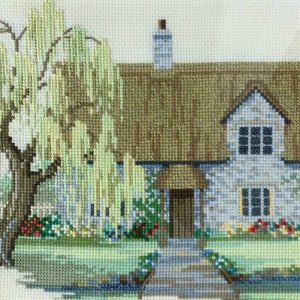 K&ouml;nnte beinhalten: Eine Kreuzstich-Stickerei, die ein Cottage mit einem Strohdach, einer Steinfassade und einer Trauerweide im Vordergrund zeigt. Das Cottage hat eine braune T&uuml;r und Fenster mit wei&szlig;en Rahmen. Die Trauerweide hat gr&uuml;ne Bl&auml;tter und &Auml;ste, die bis zum Boden h&auml;ngen.