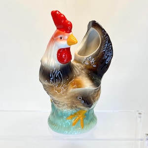 May include: A ceramic rooster planter with a brown, white and yellow glaze. The rooster has a red comb and wattle and a yellow beak. The planter has a hole in the back for drainage.