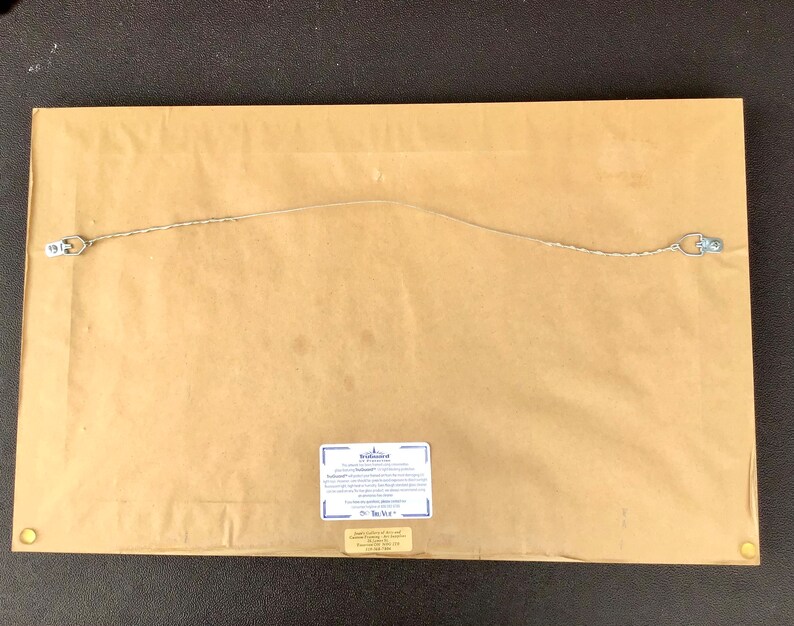 K&ouml;nnte beinhalten: Die R&uuml;ckseite eines gerahmten Drucks mit einem Echtheitszertifikat. Das Zertifikat stammt von "The Bradford Exchange" und hat einen blauen Rand. Der Druck h&auml;ngt an einer braunen Wand.