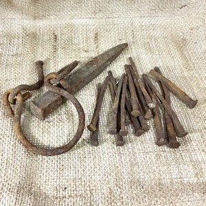 May include: A collection of rusty nails and a metal hook with a ring attached. The items are arranged on a hessian surface.