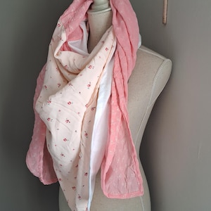 Peut inclure: Écharpe superposée rose et crème, drapée sur un mannequin. Le motif floral est sur fond crème, avec des sections roses unies. Le tissu semble doux et léger, idéal pour le printemps ou l'été.