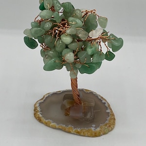 Könnte beinhalten: Eine dekorative Baumskulptur mit einem Kupferdrahtstamm und Ästen, verziert mit grünen und weißen Edelsteinblättern. Der Baum steht auf einer Basis aus natürlicher Achatscheibe.