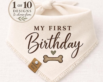 May include: An off-white triangular pet bandana with frayed edges, featuring the dark brown text "MY FIRST Birthday" above a small green heart and a brown dog bone graphic. A small brown leather-like tag labelled "Whitney Grey" is attached.