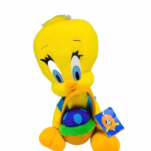 Könnte beinhalten: Gelbes Tweety Bird Plüschtier, das einen blauen und grünen Osterkorb mit einem violetten Ei darin hält. Das Spielzeug trägt ein blau-weiß gestreiftes Hemd und ein Etikett mit der Aufschrift "Looney Tunes".