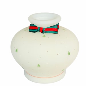 May include: A white ceramic vase with a red and green bow. The vase is decorated with small green trees and white dots.