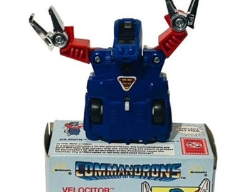 May include: A blue and red toy robot with motorized action. The robot is holding its arms up in the air. The robot is on a box that says "Commandrõns Velocitor™" and "Motorized Action".